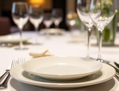 Formal dining table setting with white ceramic plates, wine glasses, and polished cutlery.